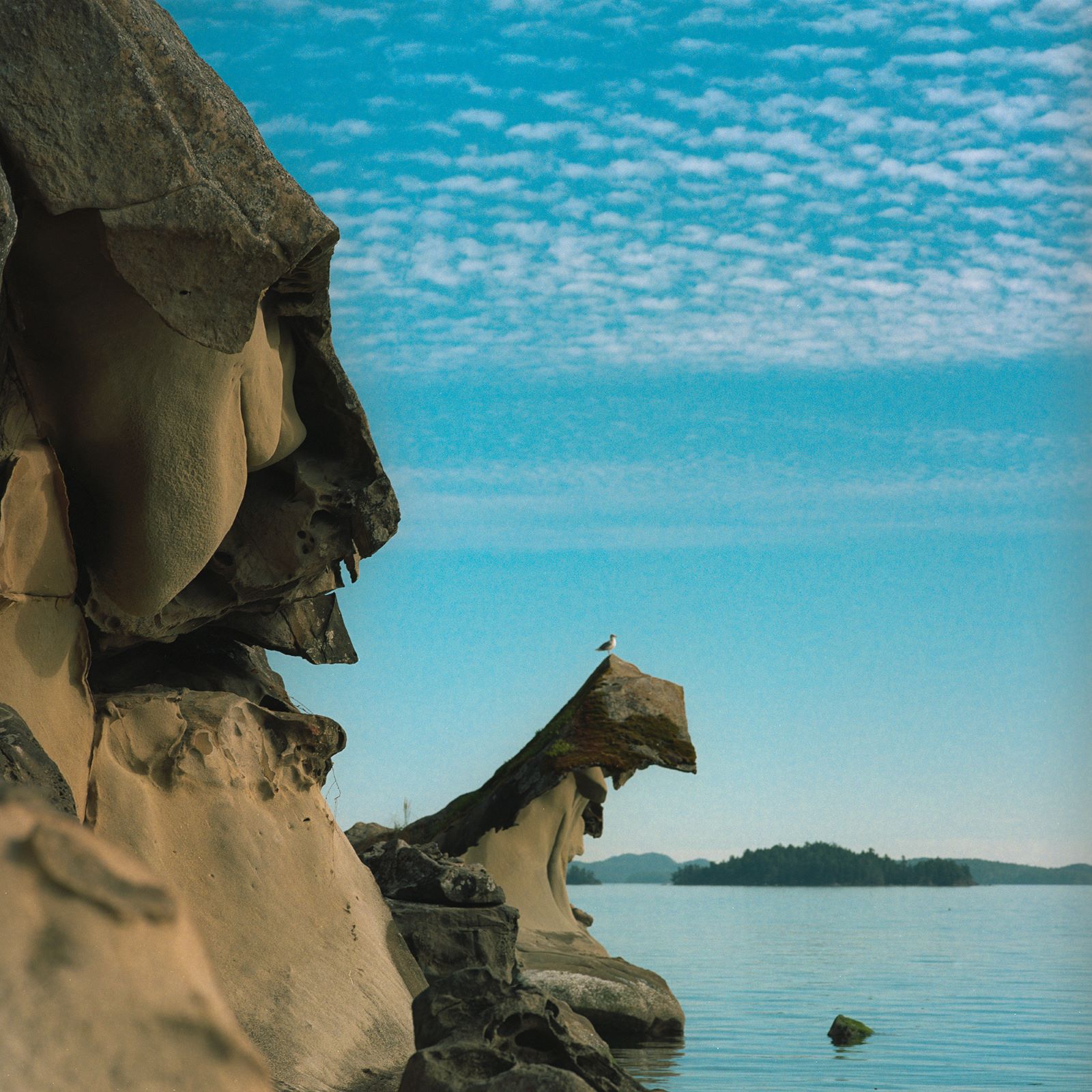 Steep sandstone shoreline with a profile of a human face against a bright blue sky